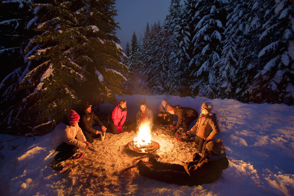Friends gathered around a bonfire in the snow at night