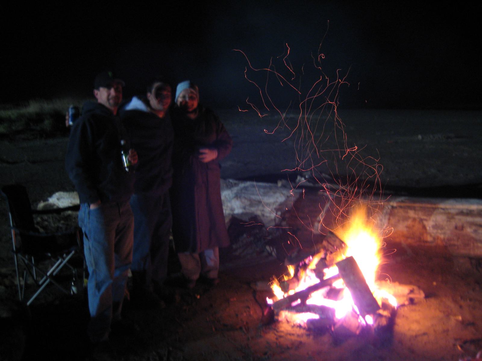 A group gathered around a bonfire at night on the shoreline